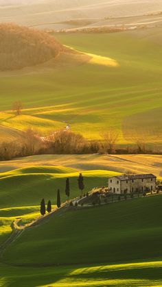 the rolling hills are covered in green grass and there is an old house on top