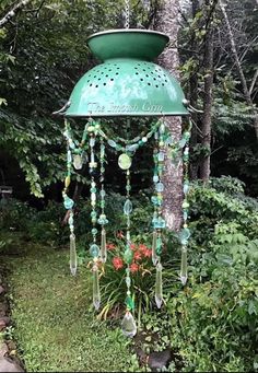 a green lamp hanging from the side of a tree in a garden with flowers and plants around it