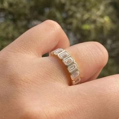 a person's hand holding a ring with three stones on it, in front of some trees