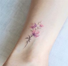 a small flower tattoo on the ankle that is pink and has purple flowers growing out of it