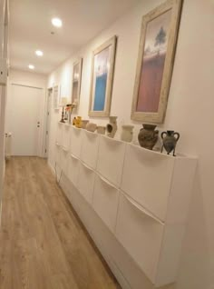 a hallway with white cabinets and vases on the wall, along with hardwood flooring