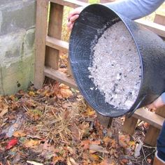 a woman is holding a bucket full of dirt in front of a brick wall and fence