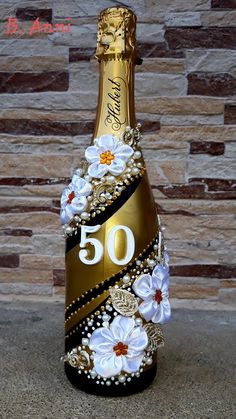 a 50th birthday cake shaped like a bottle with flowers and pearls on the top, sitting in front of a brick wall