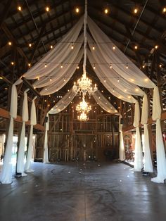 the inside of a barn with white drapes and chandelier