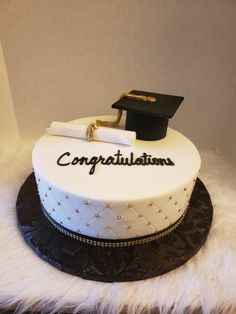 a graduation cake with congratulations written on the side and a mortar cap atop it, sitting on a white furnishing