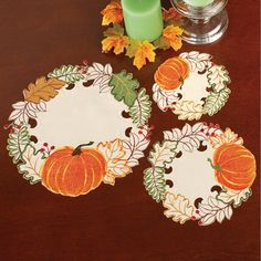 three plates with pumpkins and leaves on them sitting on a table next to a candle