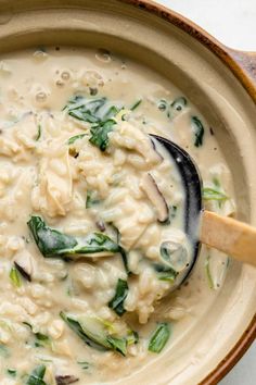 a bowl filled with pasta and spinach on top of a white countertop next to a wooden spoon