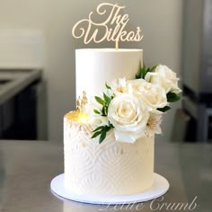 a white wedding cake with flowers and the words the wishes on top is sitting on a table