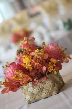 a basket filled with pink and yellow flowers on top of a white table cloth covered table