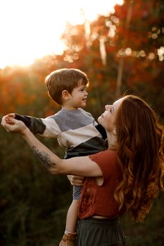 a woman holding a young boy in her arms as the sun sets behind them,