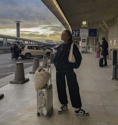 a woman is standing next to her luggage at the airport with cars in the background