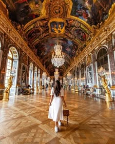 a woman in a white dress is walking through an ornate hall with paintings on the ceiling