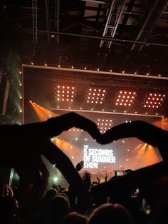 the crowd is at a concert with their hands in the shape of a heart