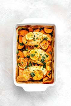 a casserole dish filled with chicken, potatoes and lemons on a white surface