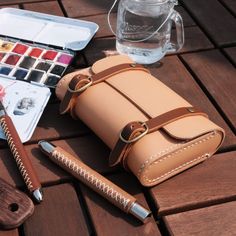 a brown leather case sitting on top of a wooden table next to a bottle of water