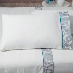 two pillows on top of a bed with white sheets and blue trims next to a vase