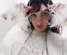 a woman with white feathers on her head and sweater over her shoulders, posing for the camera