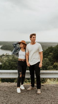 a man and woman standing next to each other on top of a hill with trees in the background