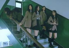 four girls in school uniforms are standing on the stairs