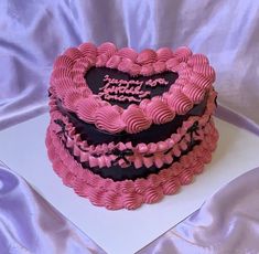 a heart shaped cake sitting on top of a white tablecloth covered table with pink and black frosting