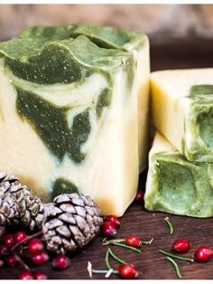 soap bars with pine cones and berries on the table next to it are two pieces of soap that have green leafy designs on them