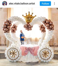 a man standing behind a table with balloons on it and a crown above the table