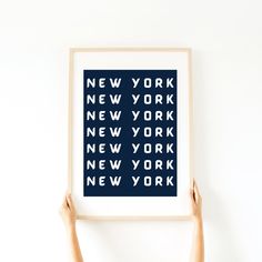 two hands holding up a blue and white art print with the words new york on it