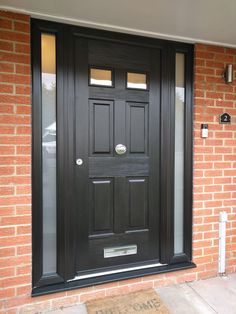 a black front door with two sidelights on the brick wall next to a welcome mat