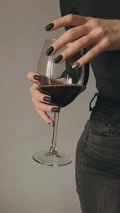 a woman holding a wine glass in her right hand and wearing black nail polishes