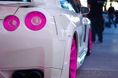 the rear end of a white sports car with pink lights on it's bumper