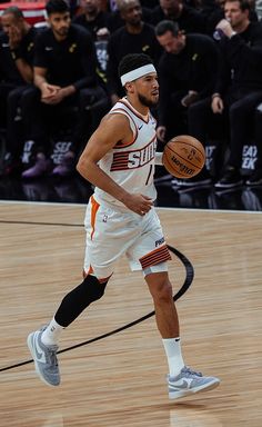 a basketball player dribbles the ball while onlookers watch from the sidelines