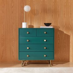 a green chest of drawers sitting on top of a wooden floor next to a lamp