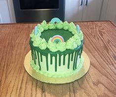 a birthday cake with green icing and a rainbow on the top is sitting on a wooden table