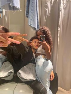 a man and woman taking a selfie in front of a bathroom mirror with clothes hanging on the wall