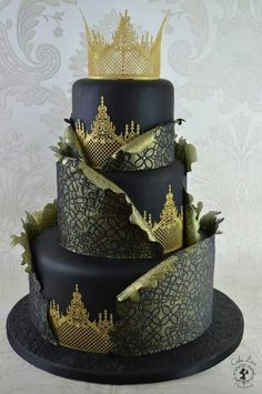 a three tiered cake decorated with gold and black icing, topped with a crown