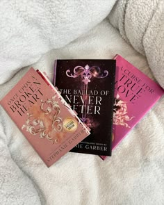 three books sitting on top of a bed next to each other in front of a white blanket