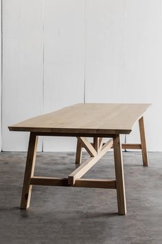 a wooden table sitting on top of a cement floor next to a white painted wall