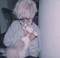 a woman holding a white and grey cat in her arms while wearing a gray sweater