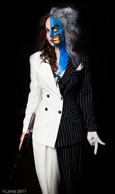 a woman in a white suit and blue face paint holding an umbrella while standing next to a man with grey hair