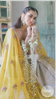 a woman in a yellow sari sitting on a chair with flowers around her neck