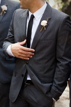 two men in suits with boutonnieres on their lapels, one wearing a flower