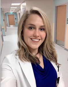 a woman in a white blazer and blue top smiling at the camera with her hands on her hips