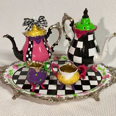 two teapots on a tray decorated with colorful designs and bows are sitting next to each other