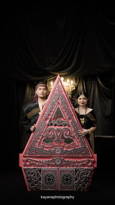 two people standing next to a red and silver object in the shape of a triangle