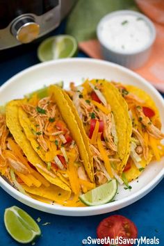 shredded chicken tacos in a white bowl with limes and tomatoes on the side