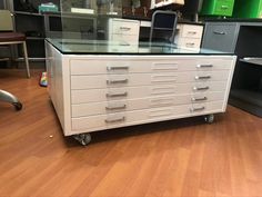 a white dresser with drawers and glass top on wheels in a room filled with other furniture