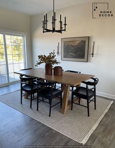 a dining room table with black chairs and a vase on top of it, in front of a large window