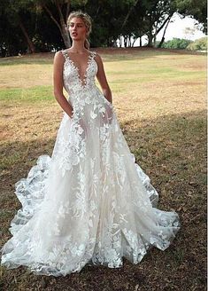 a woman standing in the grass wearing a wedding dress with an open back and floral appliques