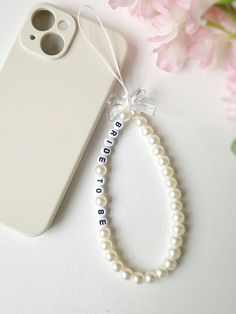 Elevate your phone's style with our custom pearl phone charm. Crafted with beautiful pearls and accented with a charming bow bead, this accessory adds a touch of elegance to your everyday look. Personalize your phone charm to make it uniquely yours. It can be used as a phone chain, phone keychain, or even a phone bracelet. Both functional and fashionable, it's an ideal gift for yourself or a friend. Embrace the trend of beaded phone straps with our customizable pearl phone charm today. Bracelet Telephone Perle, Bracelet Telephone, Phone Chain Beads, Pearl Phone Charm, Phone Bracelet, Phone Keychain, Phone Straps, Phone Chain, Custom Keychain