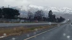 a car driving down the road in front of snow covered mountain range on a cloudy day